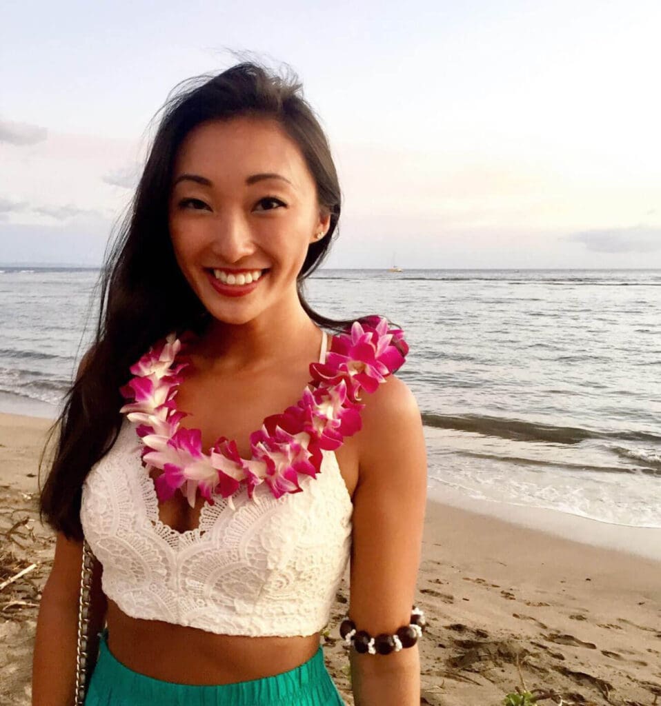 Girl on the beach smiling at the camera with a Hawaiian flower lei around her neck