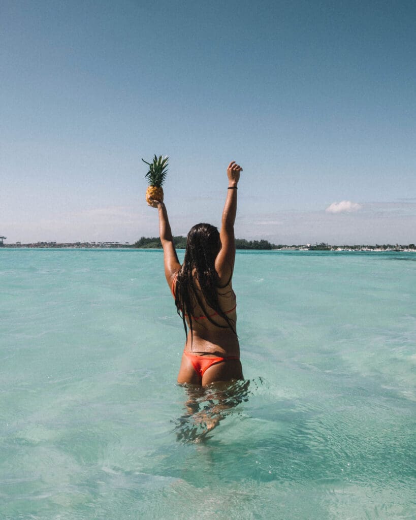 Girl in bikini with hands up holding a pineapple