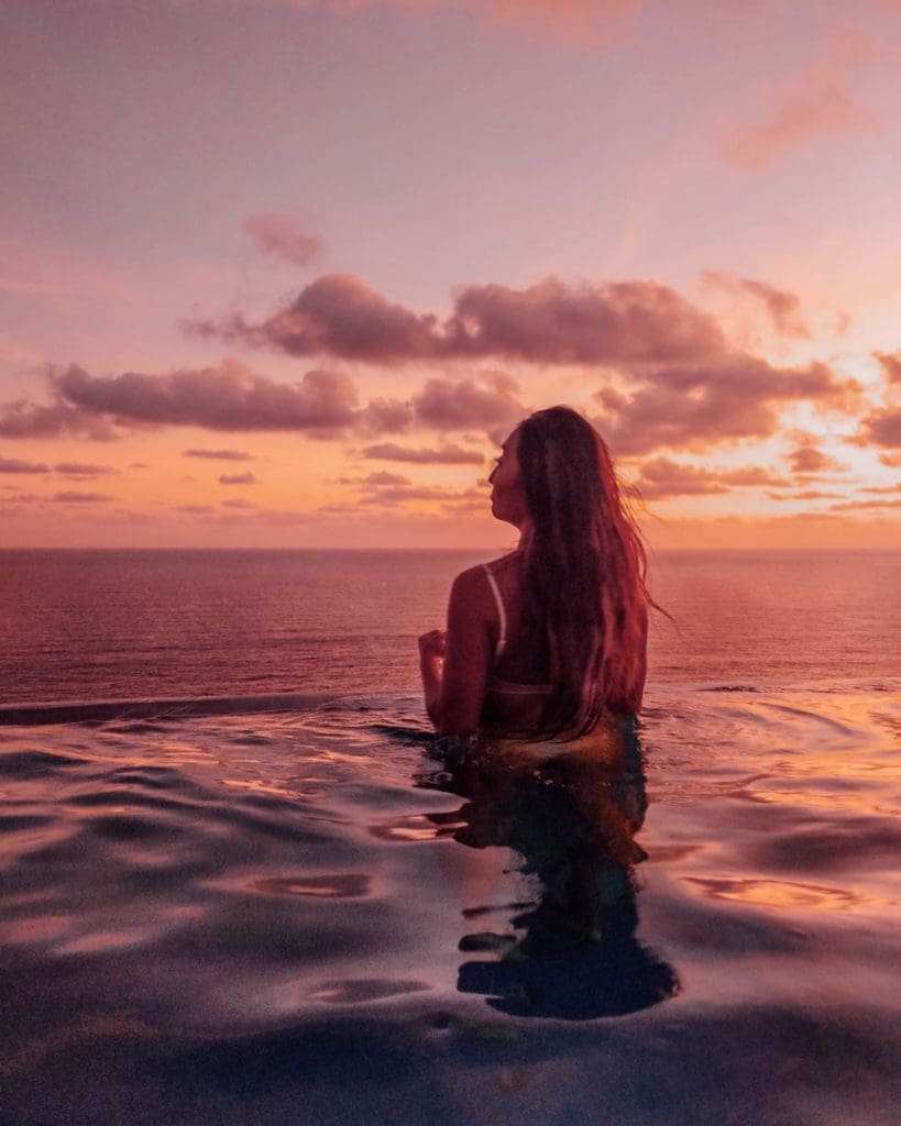 Girl in an infinity pool on a cliff overlooking the ocean during sunset