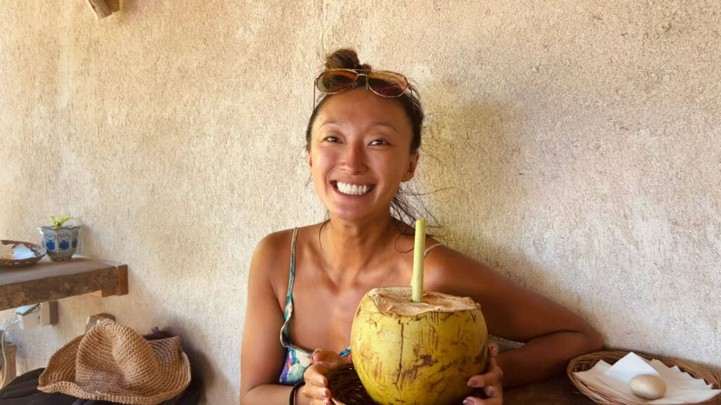Girl smiling at the camera with a coconut in front of her at a health food restaurant in Rote Island