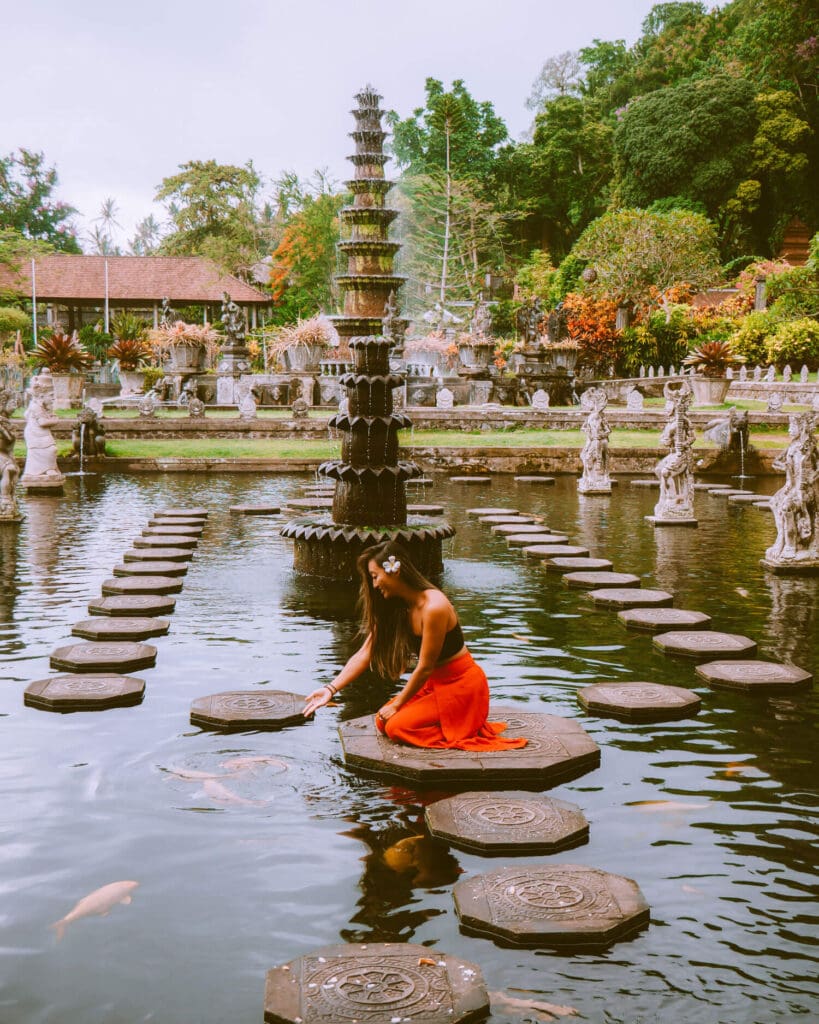 Woman kneeling and reaching down to feed fish at a Balinese temple