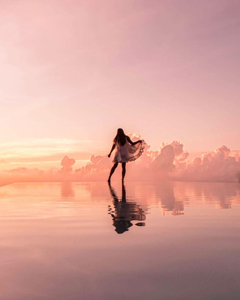 Girl standing at the edge of an infinity pool with reflections of clouds